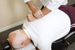 Chiropractor giving back adjustment on senior citizen.
